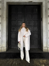a lady wears a white oversized wool coat with white pants